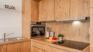 A modern kitchen with wooden cabinets, stainless steel appliances, and a black induction cooktop. - "exklusives 61m² Apartment mit Haff-blick Ruhige Lage Balkon & Wlan Stellp (Zirchow)