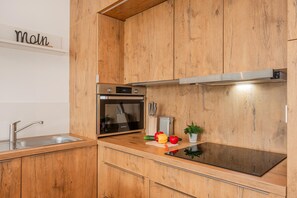 A modern kitchen with wooden cabinets, stainless steel appliances, and a black induction cooktop. - "exklusives 61m² Apartment mit Haff-blick Ruhige Lage Balkon & Wlan Stellp (Zirchow)