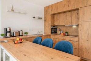Een moderne keuken met houten kastjes, een inbouwoven en een eethoek met blauwe stoelen.
