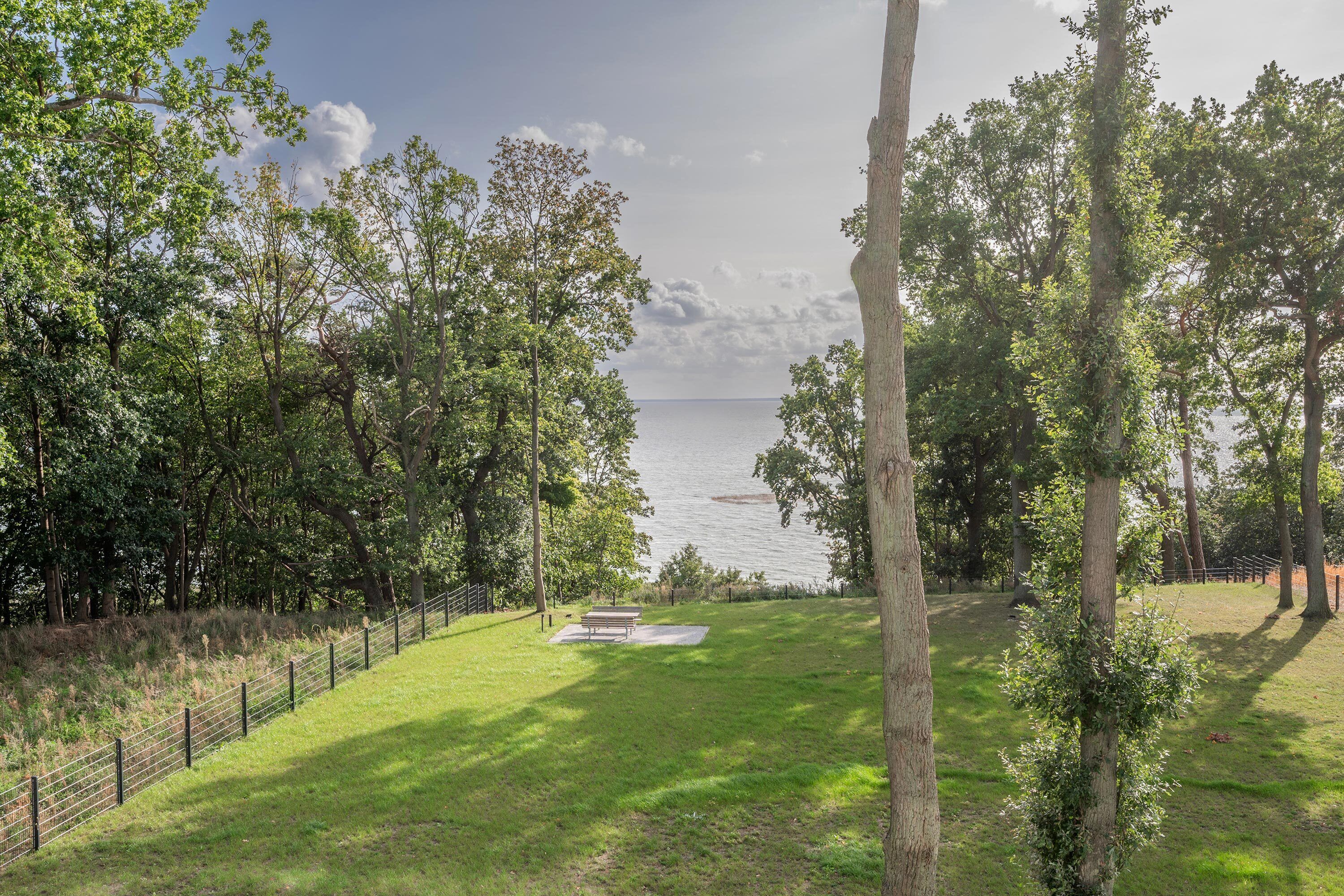 A grassy area with a bench and a fence, overlooking a body of water.