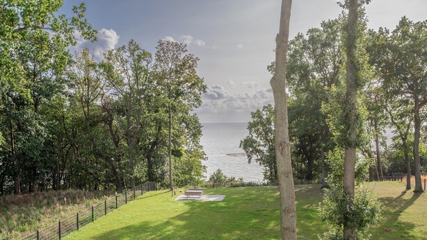 A grassy area with a bench and a fence, overlooking a body of water. - "exklusives 61m² Apartment mit Haff-blick Ruhige Lage Balkon & Wlan Stellp (Zirchow)