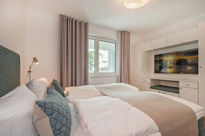 Een hotelkamer met twee bedden, een televisie, een raam met gordijnen en een lamp.