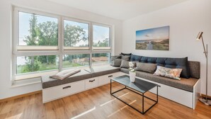 A modern living room with a large window, a sofa with storage, a coffee table, and a painting on the wall.