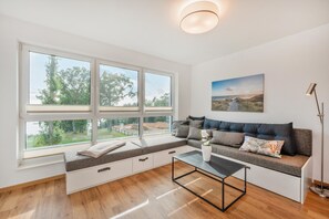 Un salon moderne doté d’une grande fenêtre, d’un canapé avec espace de rangement, d’une table basse et d’un tableau accroché au mur.