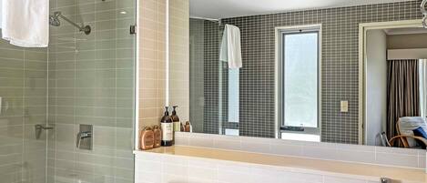 Ein modernes Badezimmer mit Duschkabine aus Glas, Toilette in Weiß, Waschbecken mit Spiegel und Pflegeutensilien auf der Ablagefläche.