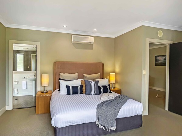 Camera d'albergo ordinata con un letto grande, due comodini con lampade, uno specchio e un condizionatore d'aria a parete.