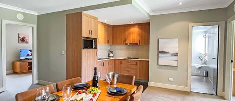 A modern kitchen with wooden cabinets, a dining area with a table set for four, and a view of the sea through a glass door.