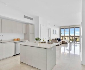 Uma cozinha moderna com armários brancos, uma ilha central e uma área de refeições com uma janela grande.