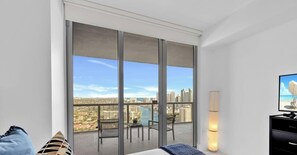A modern hotel room with a large sliding glass door leading to a balcony with a city view.