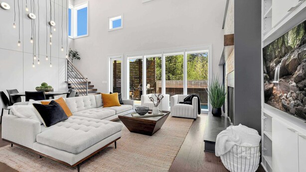 A spacious living room with a sectional sofa, a coffee table, and a large window with a view of trees.