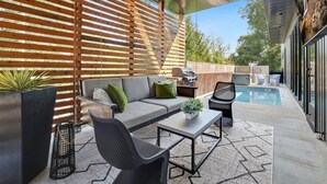 An outdoor patio with a sofa, chairs, a table, and a pool.
