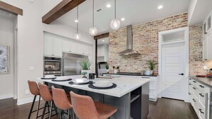A modern kitchen with a large island, pendant lights, and a brick accent wall.