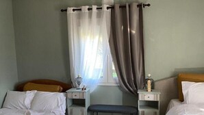 A bedroom with two single beds, a bench, a window with curtains, and a hanging lamp.