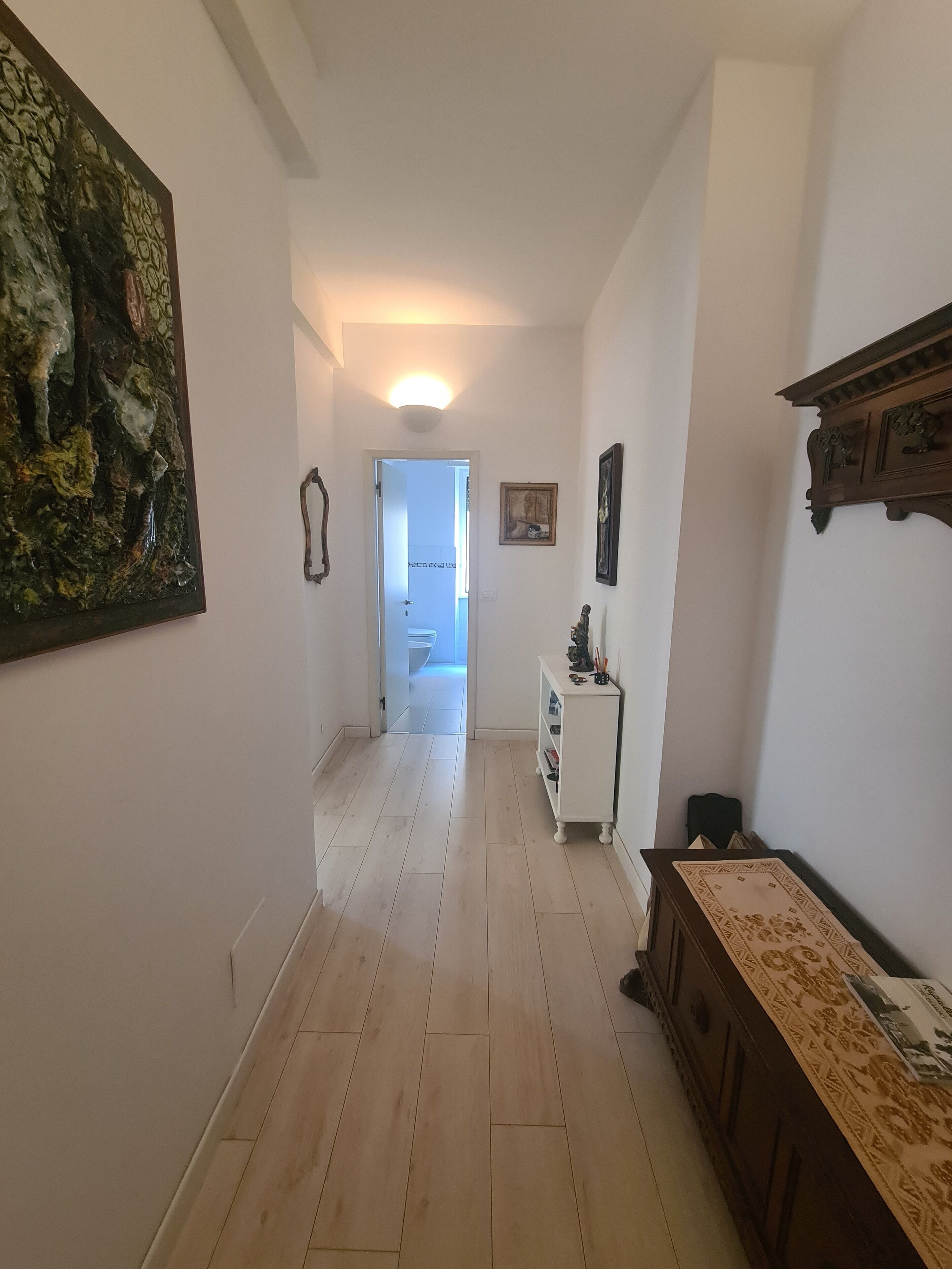 A hallway with a wooden floor, a white wall, and a door leading to a bathroom.