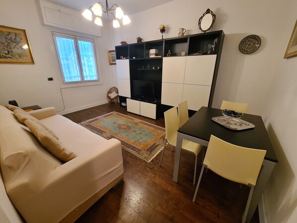Un salon avec un canapé, une table à manger et des chaises, un téléviseur et un tapis à motifs.