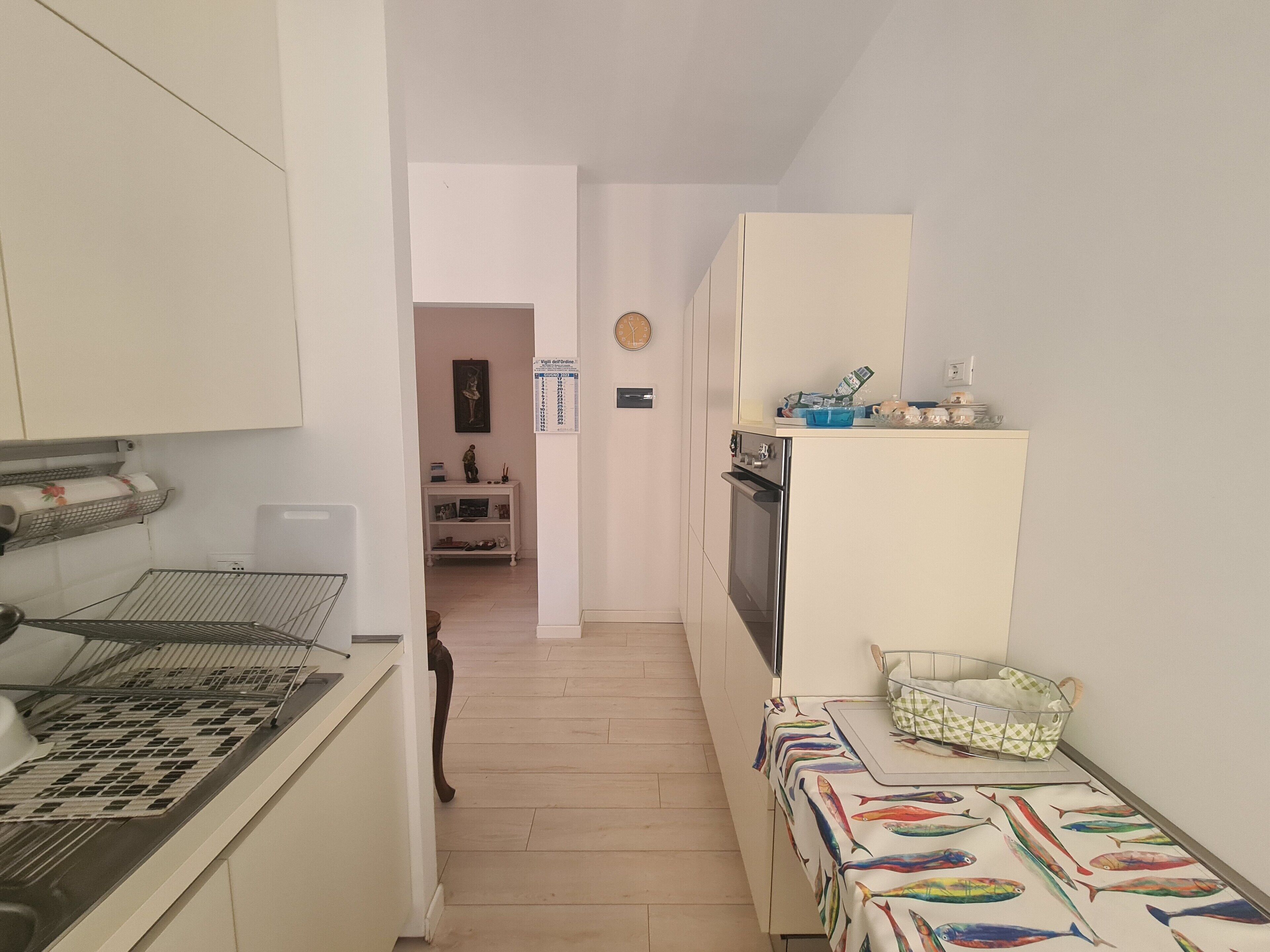 A narrow kitchen with a stove, sink, and a small dining area with a table and chairs.