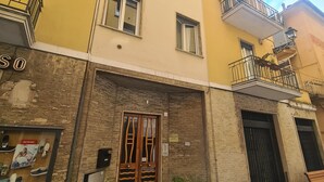 A two-story building with a yellow facade, a wooden door with glass panels, and a small balcony with metal railings. - Casa Stefania by PortofinoVacanze (Rapallo)
