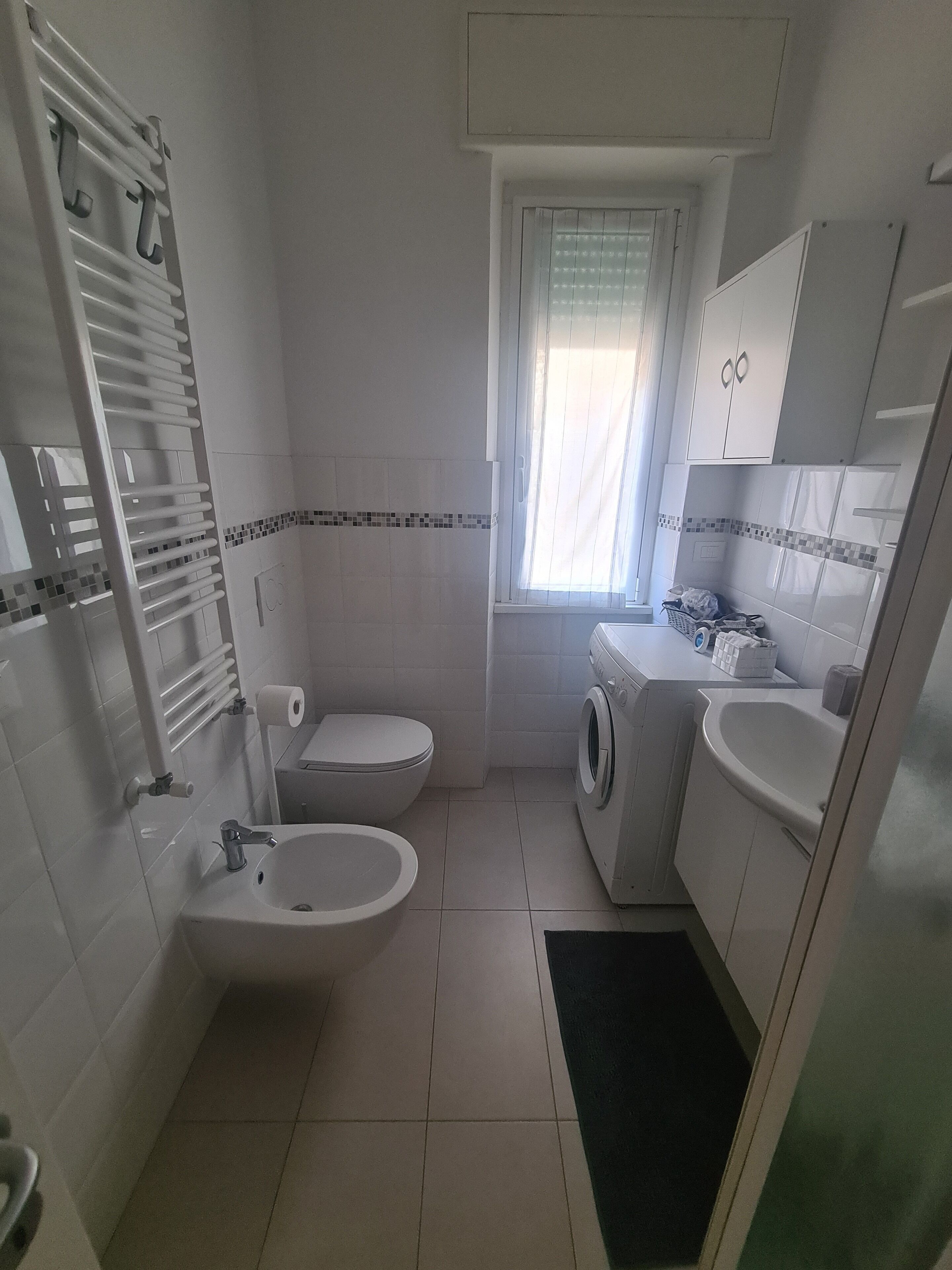 A compact bathroom with a toilet, sink, washing machine, and a small window.
