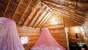 Habitació amb teulada de palla, bigues de fusta i un llit amb dosser rosa.