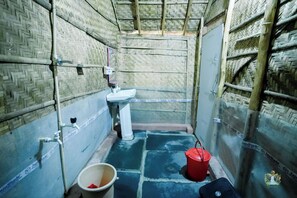 Un baño pequeño y estrecho, con un lavabo blanco y un cubo rojo sobre el suelo.