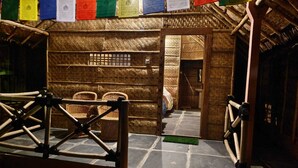 Una estructura de fusta tradicional amb un teulat de palla, una paret trenada i una porta que condueix a un espai interior.