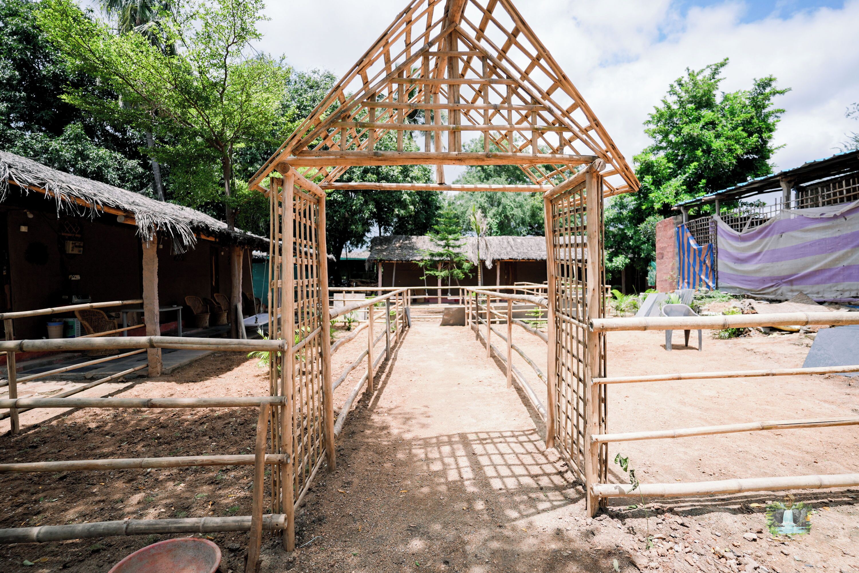 A bamboo structure with a thatched roof, surrounded by dirt paths and simple huts.