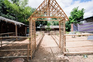 Una estructura de bambú con techo de paja, rodeada de senderos de tierra y chozas sencillas.