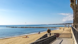 A beach with a wooden walkway, people relaxing, and a clear sky. - Penthouse Duplex with Panoramic Sea Views (Marbella)
