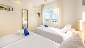 A hotel room with two beds, a ceiling fan, a large window with a view, and a mirror on the wall. - Penthouse Duplex with Panoramic Sea Views (Marbella)