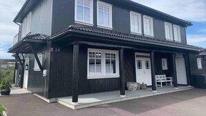 A two-story building with a dark exterior, white trim, and multiple windows. - 3-roms Leilighet på Gateplan i Landlige Omgivelser (Vestfold og Telemark,)