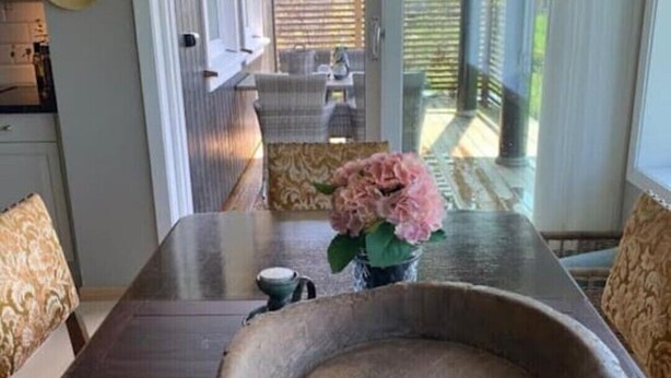 A dining area with a large stone bowl centerpiece, a vase with pink flowers, and a view of an outdoor patio with a table and chairs. - 3-roms Leilighet på Gateplan i Landlige Omgivelser (Vestfold og Telemark,)