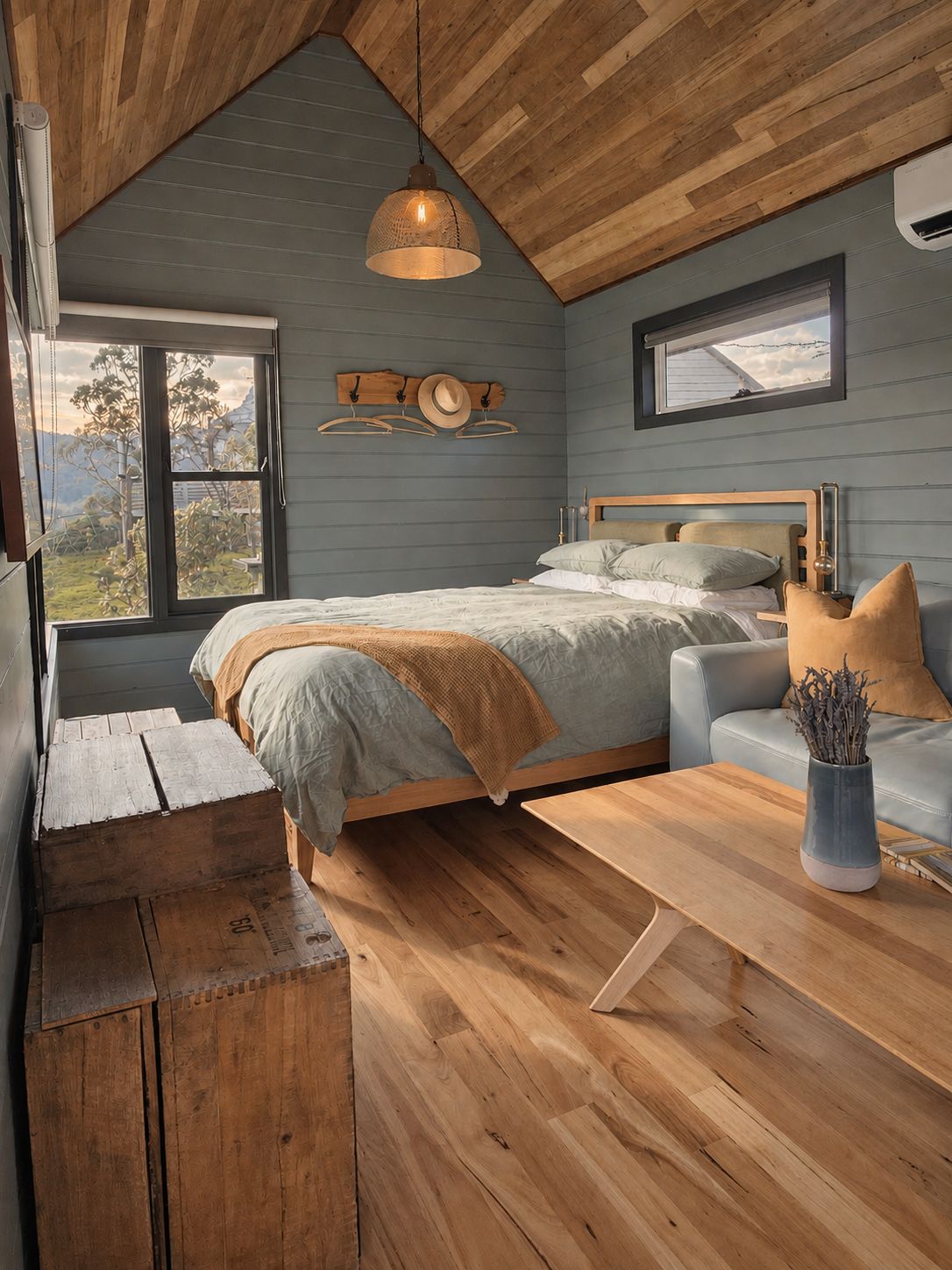 A bedroom with a bed, a wooden bench, a sofa, a table, and a hanging light fixture.