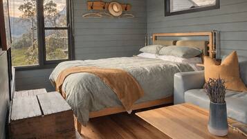 A bedroom with a bed, a wooden bench, a sofa, a table, and a hanging light fixture.