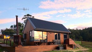 Een modern huis met een groot terras, een schoorsteen en uitzicht op de zonsondergang.
