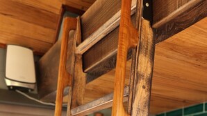 Een houten ladder staat tegen een keukenkastje met een groene tegelwand en een raam op de achtergrond.