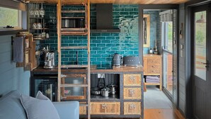 Een gezellige woonkamer met een houten plafond, een blauwe bank, een keuken met een blauwgroene tegelachtergrond en een hanglamp.