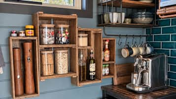 Una cocina con estantes de madera que sostienen frascos, botellas y utensilios de cocina.