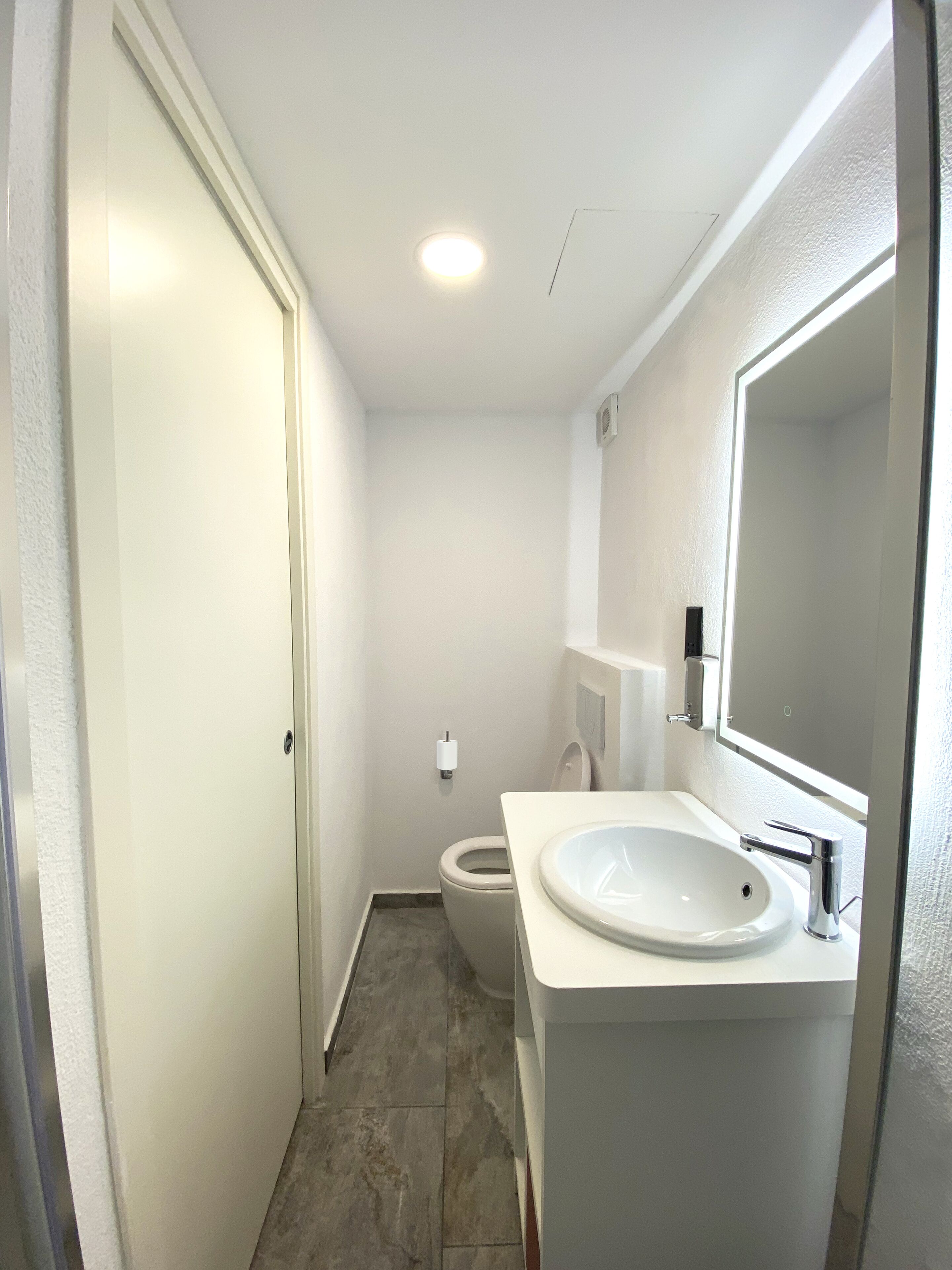 A small, clean bathroom with a toilet, sink, and mirror.
