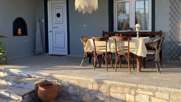 A covered outdoor dining area with a table and chairs, a hanging light fixture, and a stone-paved entrance. - TRADITIONAL VILLA ,COZY LITTLE HOUSE FOR A FAMILY, FOR FRIENDS OR COUPLES... (ΤΡΙΚΑΛΑ)