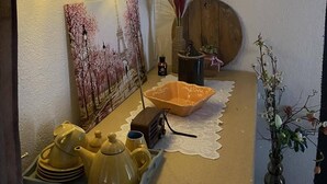 A cozy kitchen area with a wooden shelf holding kitchenware, a clock on the wall, and string lights. - TRADITIONAL VILLA ,COZY LITTLE HOUSE FOR A FAMILY, FOR FRIENDS OR COUPLES... (ΤΡΙΚΑΛΑ)