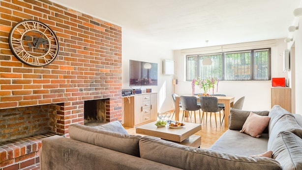 Una sala de estar con chimenea de ladrillo, un sofá, una mesa de centro con aperitivos y un televisor montado en la pared.