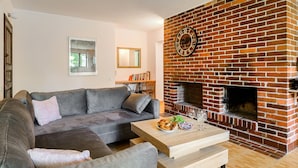 Una sala de estar con chimenea de ladrillo, un sofá gris y una mesa de centro de madera con aperitivos y vasos.