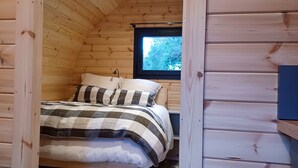 Un dormitorio acogedor tipo cabaña de madera, con cama, almohadas y ventana.