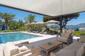 Relax by the pool with a view of the sea and distant mountains, surrounded by comfortable lounge chairs and a table.