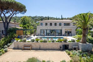 Enjoy a relaxing stay in this two-story house with a spacious outdoor area featuring a swimming pool, a bench, and lush gardens.