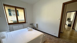A bedroom with a bed, a radiator, a window with shutters, a chair, and a hallway leading to a bathroom. - Casa Thea by PortofinoVacanze (Rapallo)