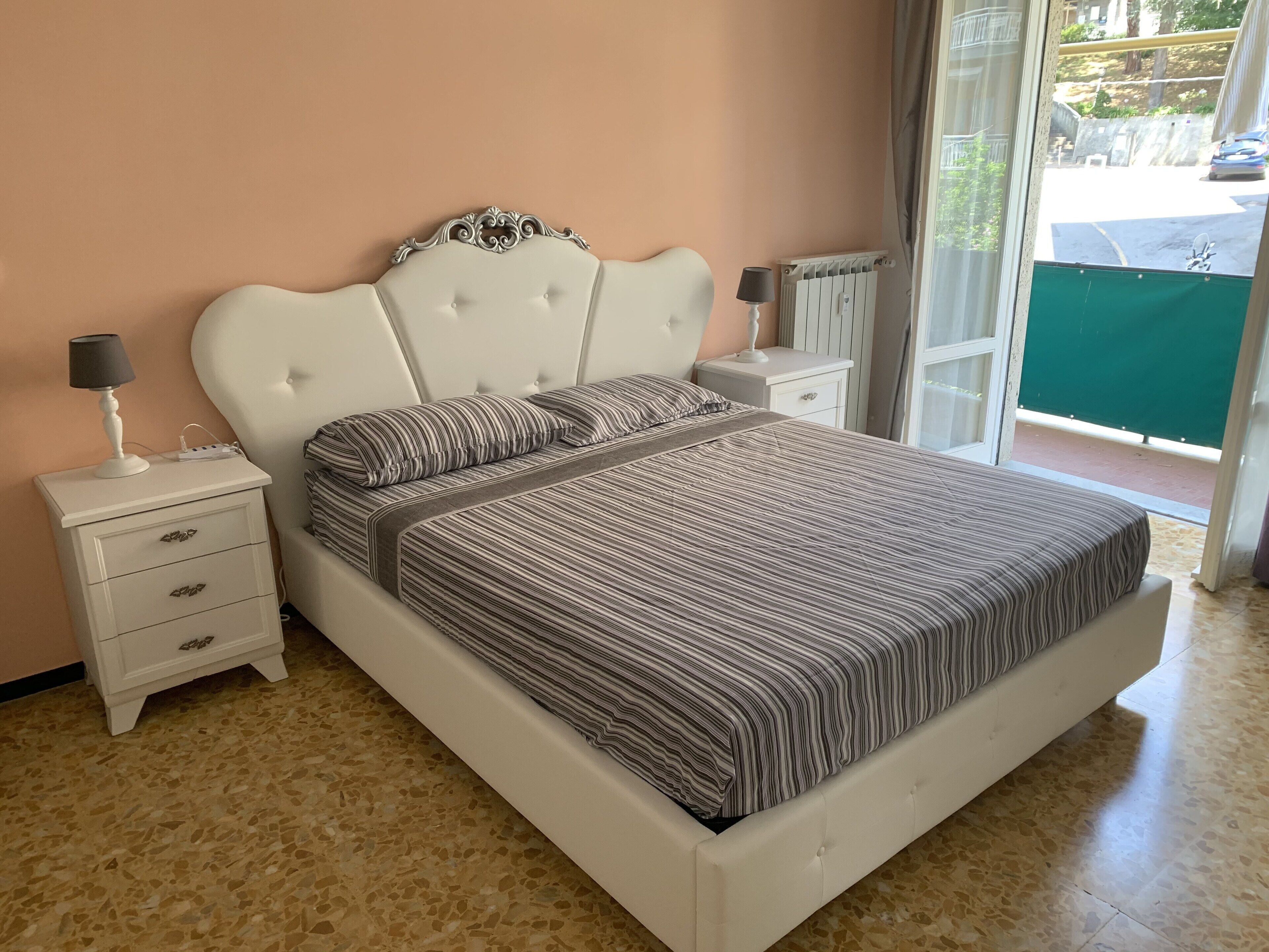 A bedroom with a bed, nightstands, and a window with a view of the street.