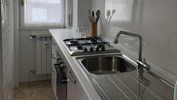 A modern kitchen with white cabinets, a gas stove, a stainless steel sink, and a window with a view of a balcony. - Casa Thea by PortofinoVacanze (Rapallo)
