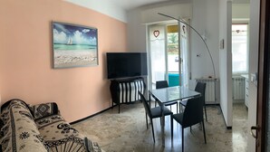 A living room with a sofa, a TV, a dining table with chairs, and a painting of a sailboat on the wall. - Casa Thea by PortofinoVacanze (Rapallo)