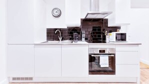 Une cuisine moderne avec des meubles blancs, un évier en acier inoxydable, un four à micro-ondes et un four traditionnel.